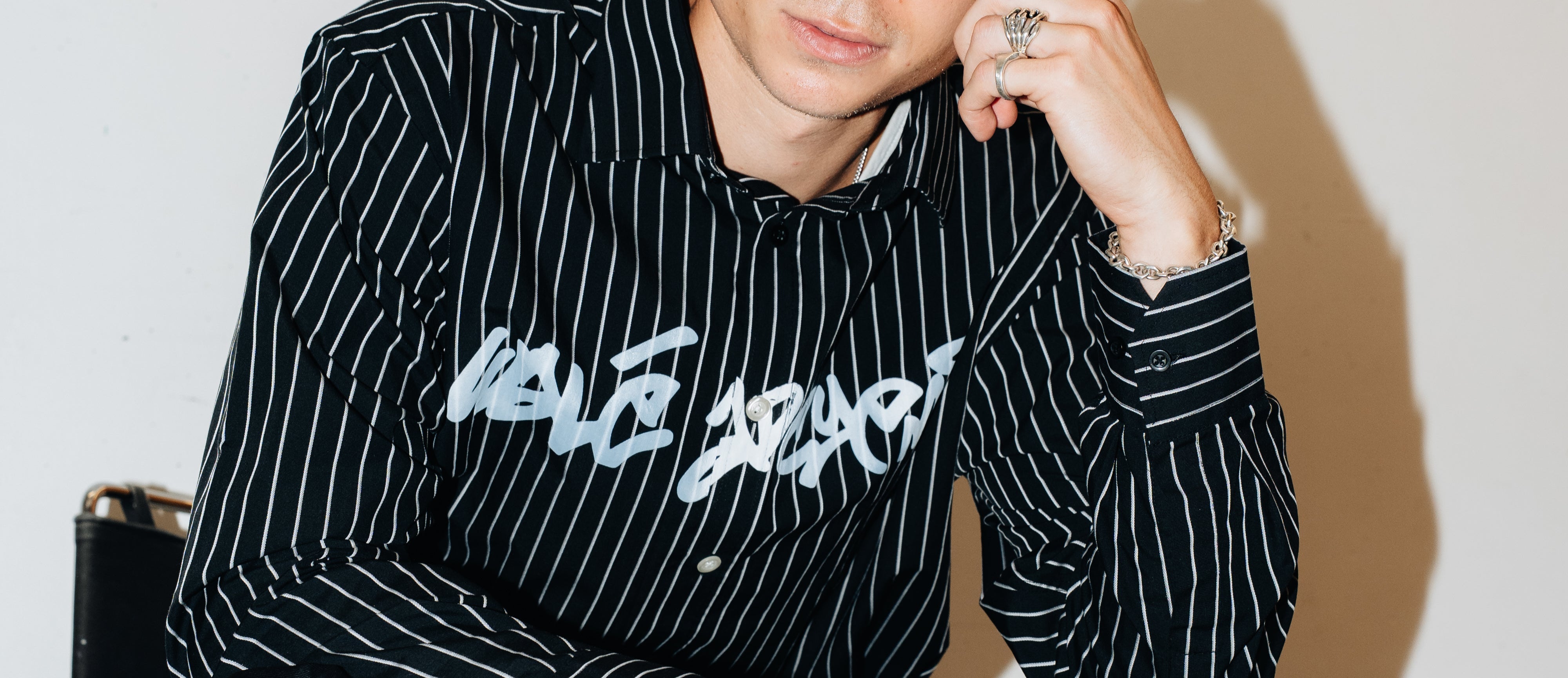 Man sitting on a chair wearing a black pinstripe shirt with white text.