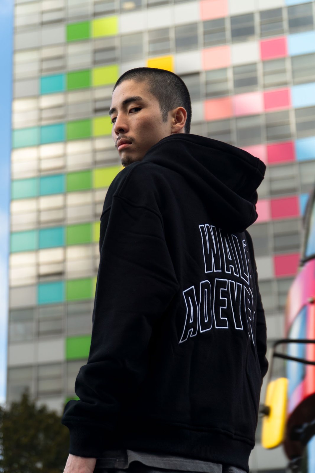 Bridge Hoodie, back, in front of a tower block