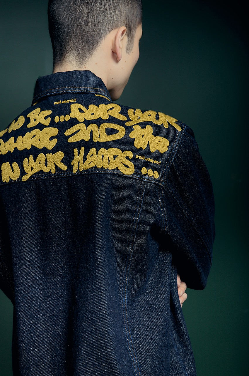Sessions denim jacket from behind, raw dark wash with the script embroidered in yellow across the yoke, Walé Adeyemi AW26
