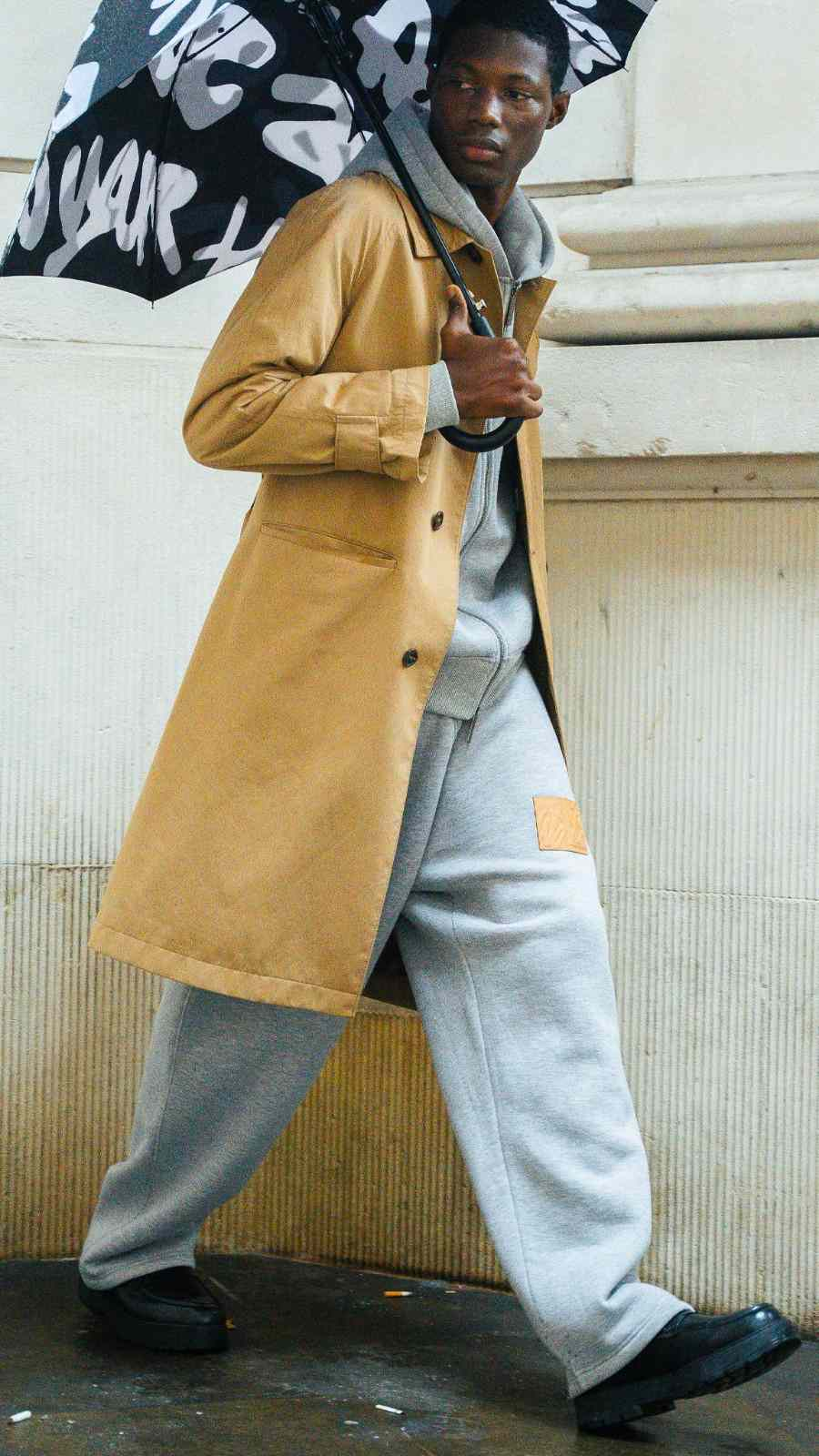 Walé Adeyemi model in tan trench coat holding a graffiti umbrella