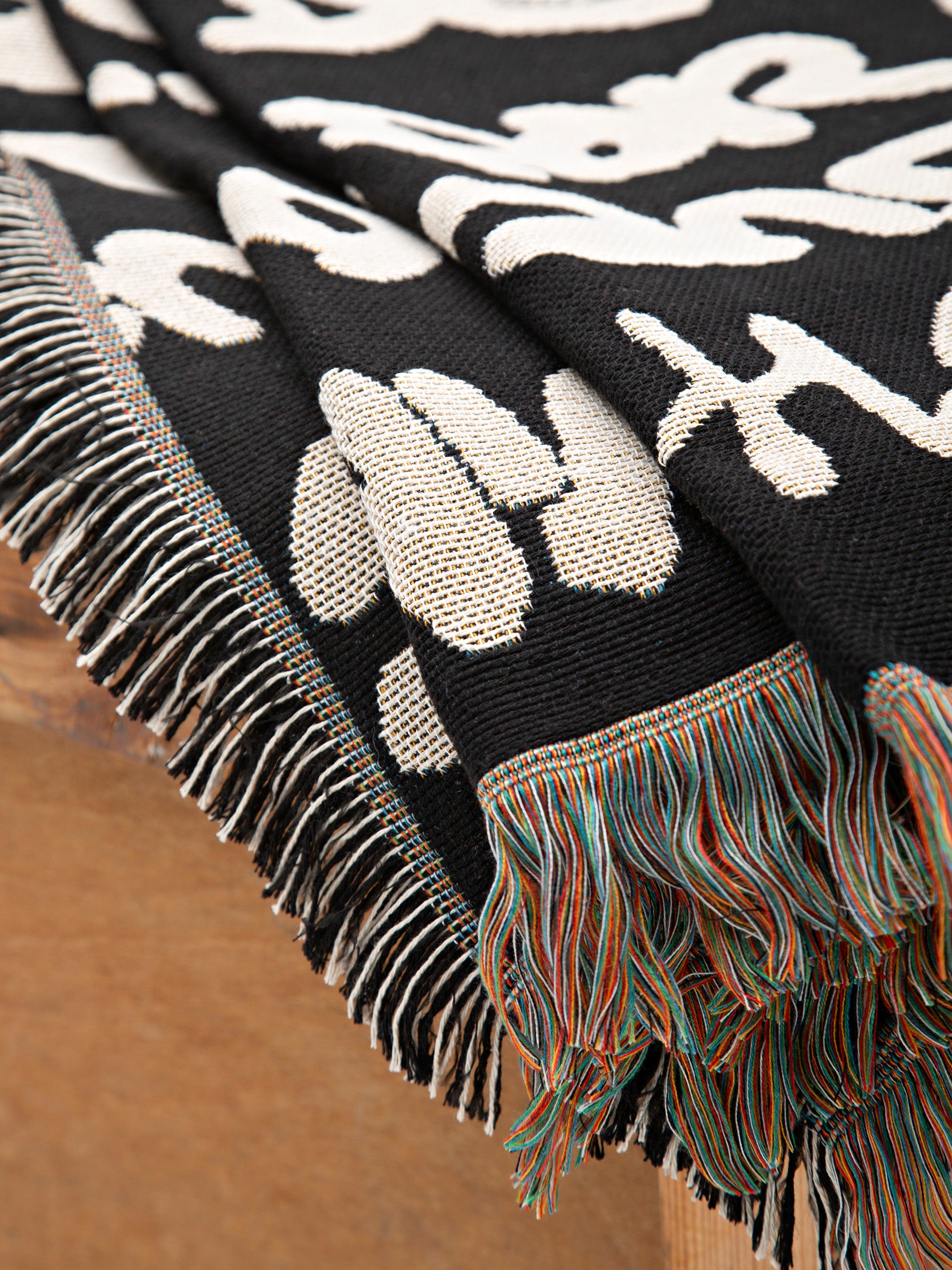 Wale Adeyemi black knit throw blanket with cream typography and colorful fringed tassels