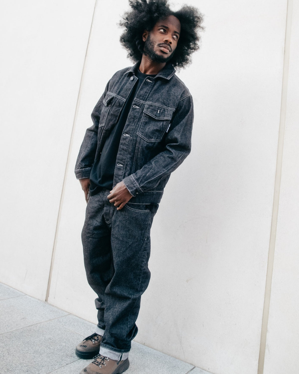 Midnight Graf Denim Jacket and jeans in Black, worn against a pale wall