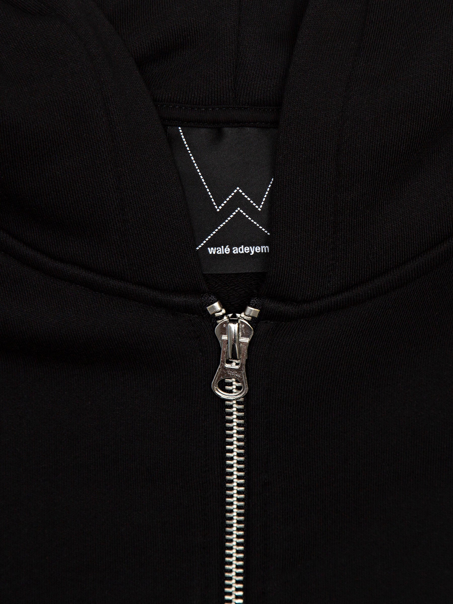 Close-up of the silver zip and walé adeyemi neck label on the Vinnie full-zip hoodie in Black/White