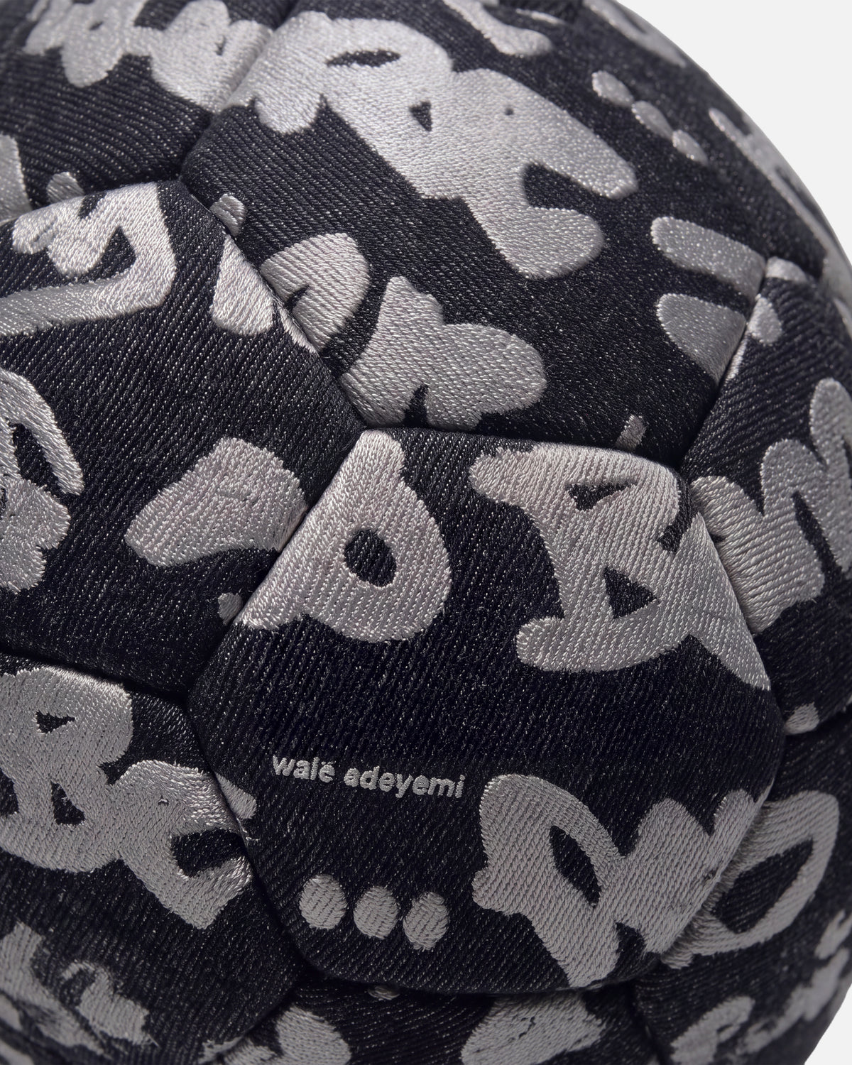 Close-up of the denim twill, grey Graf print and wordmark on the Walé Adeyemi Trivela Denim Football in Black