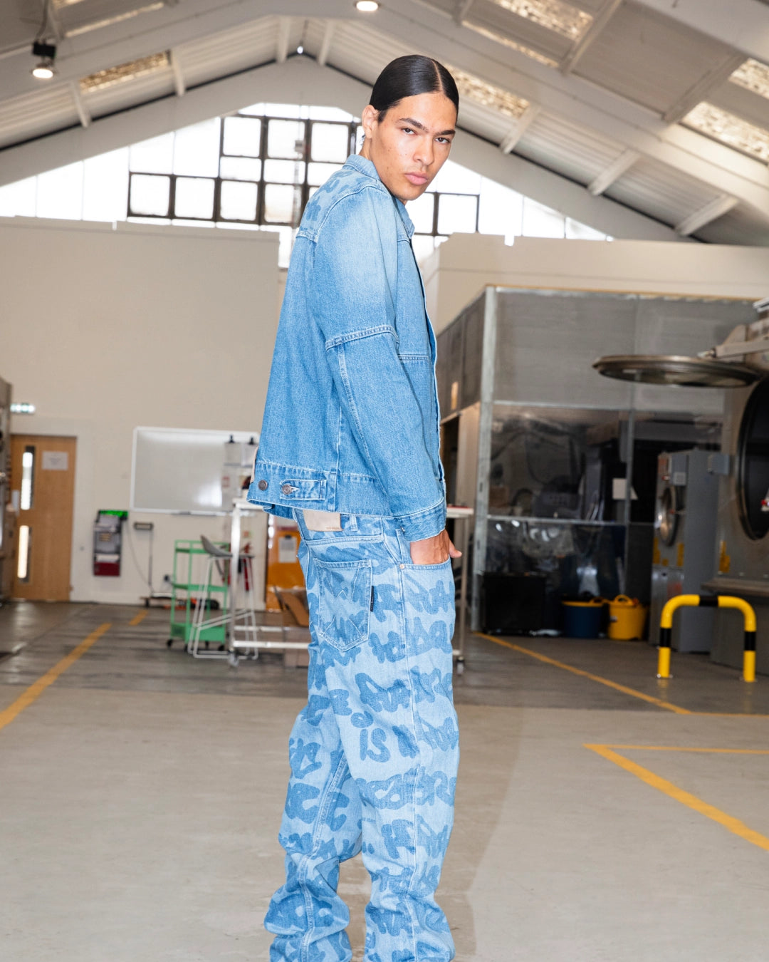 Model wearing blue denim jacket and graffiti-printed jeans in the wash area