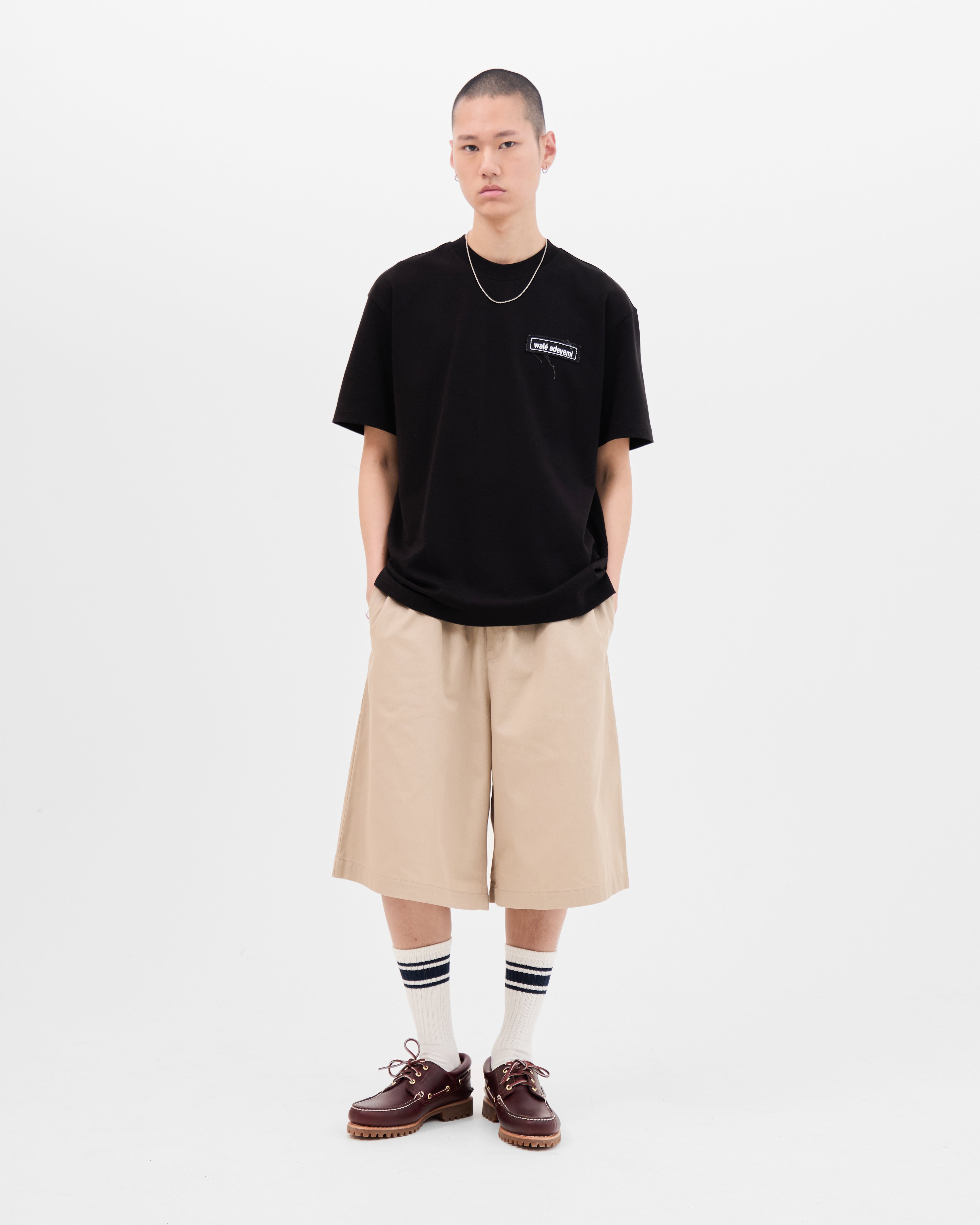 Model wearing the Walé Adeyemi Backbeat T-shirt in Black/White, full-length front view styled with beige shorts