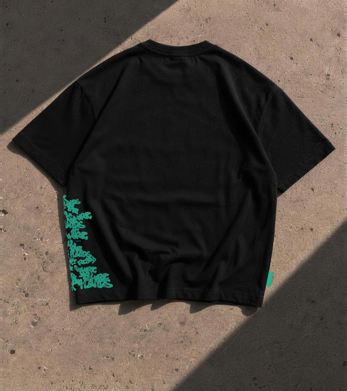 Walé Adeyemi Hendrix T-shirt in Black/Green laid flat on concrete in sunlight, back